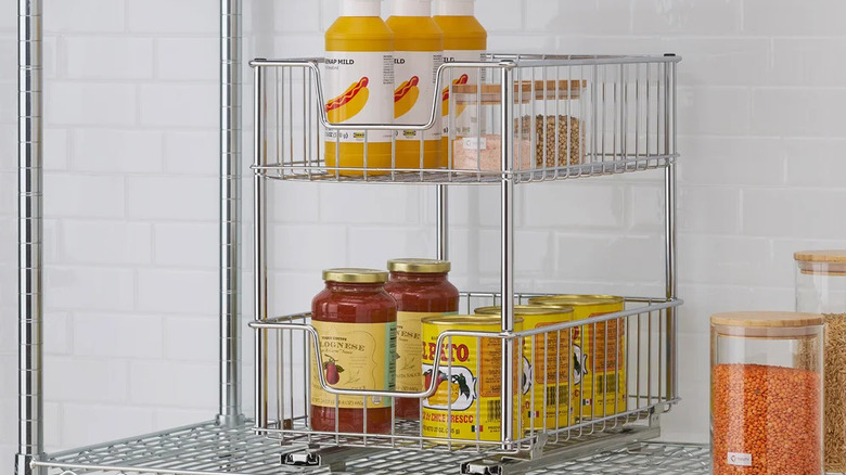 Two-tier sliding wire cabinet organizer holding jars of pasta sauce and canned goods.