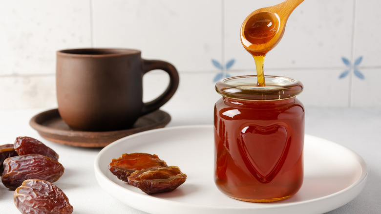 Wooden spoonful of date syrup dripping into glass jar