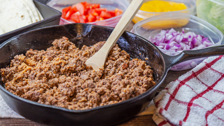 A skillet of cooked ground beef with a wooden spoon