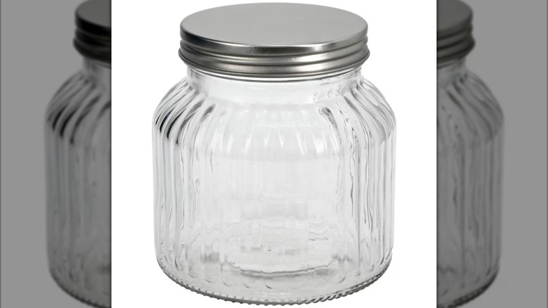 A clear, ribbed glass jar with a silver metal lid is shown against a white background