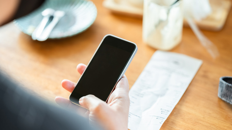 Hand holding a phone over a receipt on a restaurant table