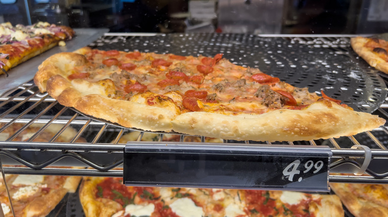 Close up view of freshly baked pizza under a warming lamp inside a pizzeria restaurant.