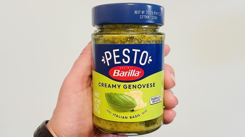 Hand holding jar of Barilla Creamy Genovese Pesto
