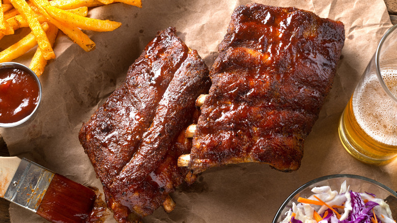 A rack of ribs on parchment paper with fries, coleslaw, and a beer
