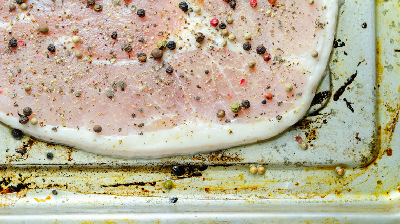 A raw piece of pork is seasoned with peppercorns and salt