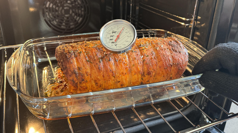 A tied pork roast in a glass dish is tested for internal temperature inside an oven