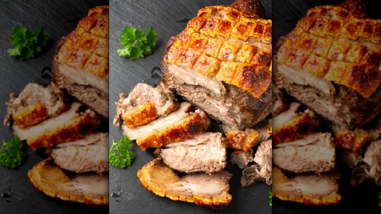 A pork roast with crispy, scored fat rests on a table
