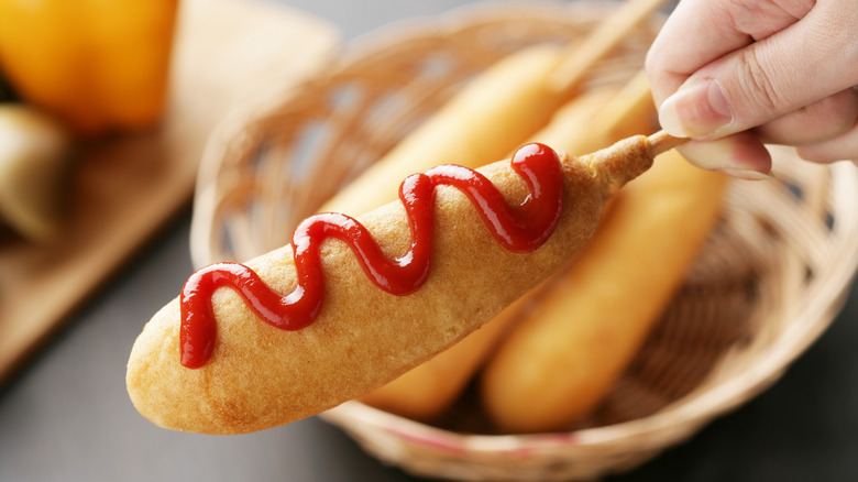 Hand holding a corn dog with a drizzle of ketchup