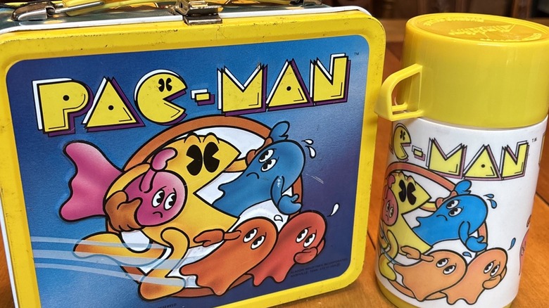 Close-up of yellow Pac-Man lunch box with matching thermos, both on wood table