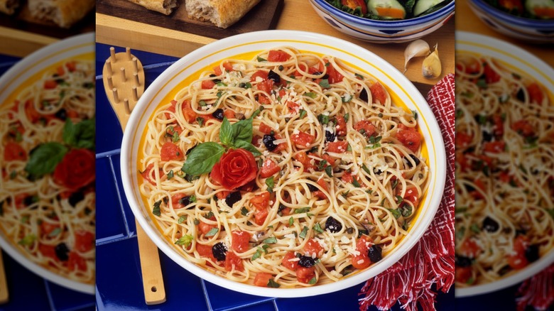 Spaghetti salad on a countertop surrounded by bread and salad