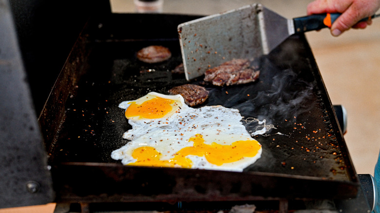 A person uses a large spatula to turn sausages and eggs on a Blackstone Griddle