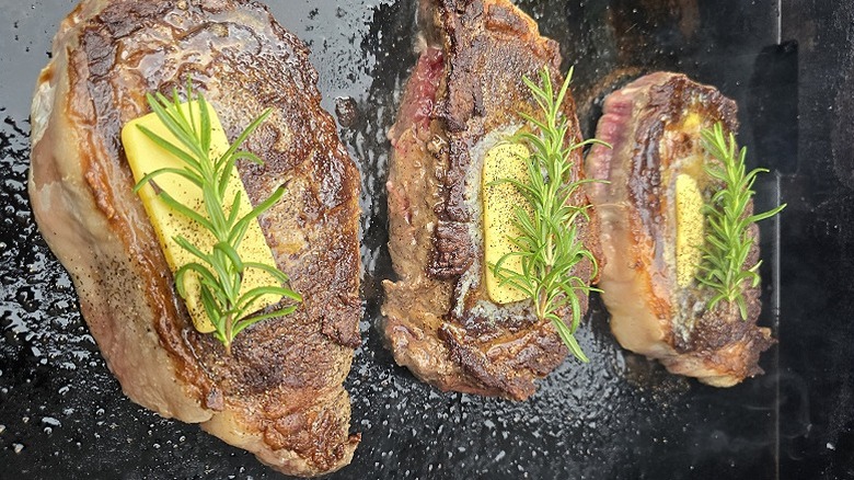 Closeup of three steaks with butter and rosemary on a Blackstone Griddle