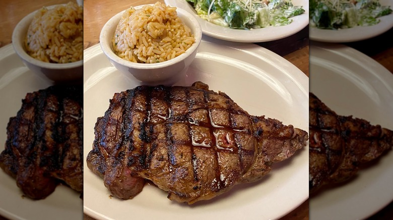 A juicy ribeye from Texas Roadhouse on white plate next to a salad and rice.