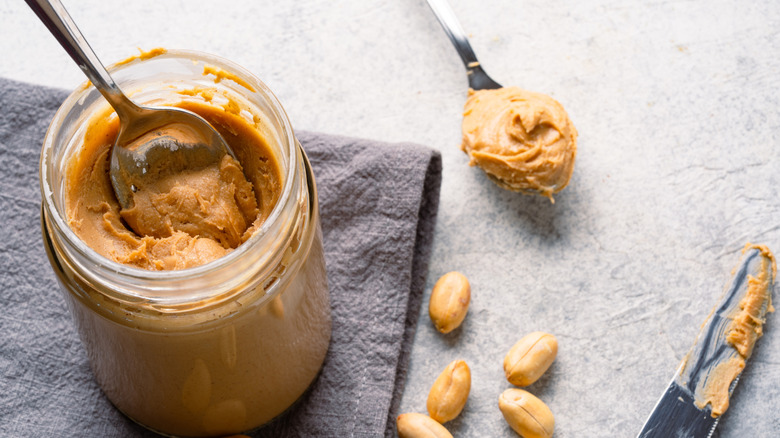 Overhead view of an open jar of peanut butter with spoons and a knife