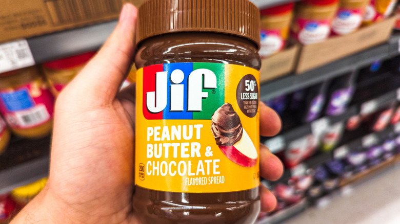 Hand holding jar of Jif Peanut Butter & Chocolate Flavored Spread in grocery store
