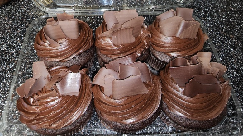 Six All-American Chocolate Cupcakes from Costco sit in a plastic clamshell container on a black cabinet