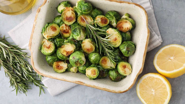 Dish of roasted Brussels sprouts with a halved lemon and fresh rosemary