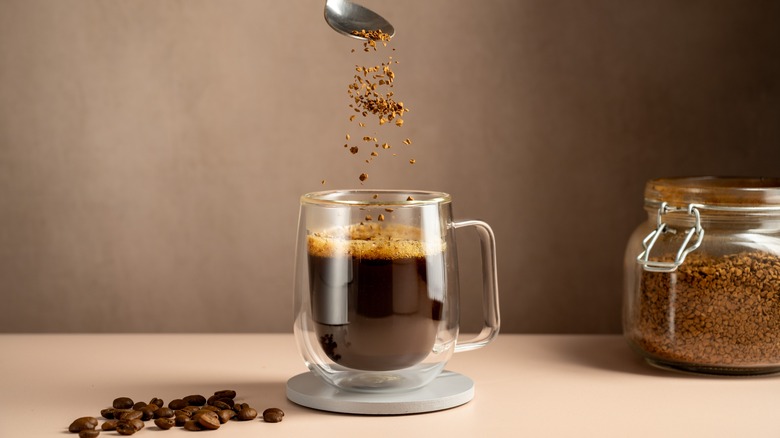 small cup of coffee in glass mug with sprinkle of coffee beans