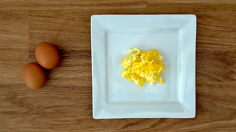 Two eggs and square white plate of scrambled eggs