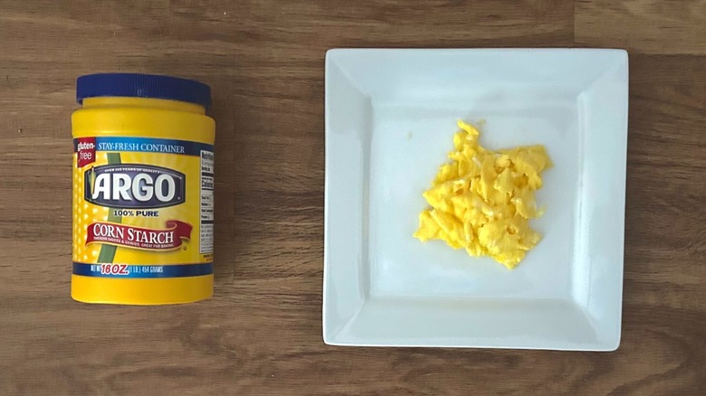 Container of cornstarch and square white plate of scrambled eggs