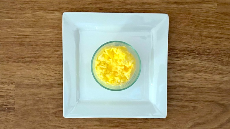 Square white plate with glass ramekin of scrambled eggs