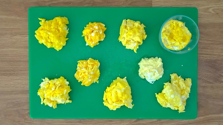 Nine different batches of scrambled eggs on a green cutting board