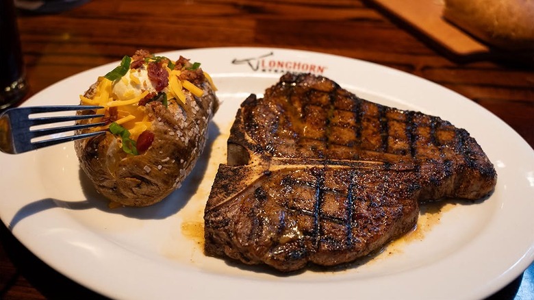 A steak and a baked potato sit on a plate.