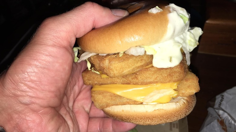 A hand holds a triple Filet-O-Fish sandwich from McDonald's