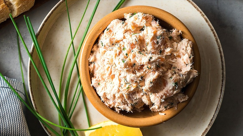 Bowl of smoked salmon dip on a plate with fresh chives and a lemon wedge