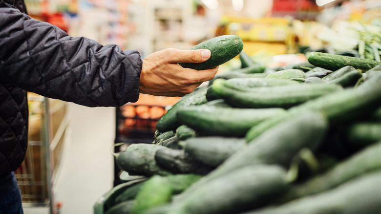Hand picking up cucumber at supermarket