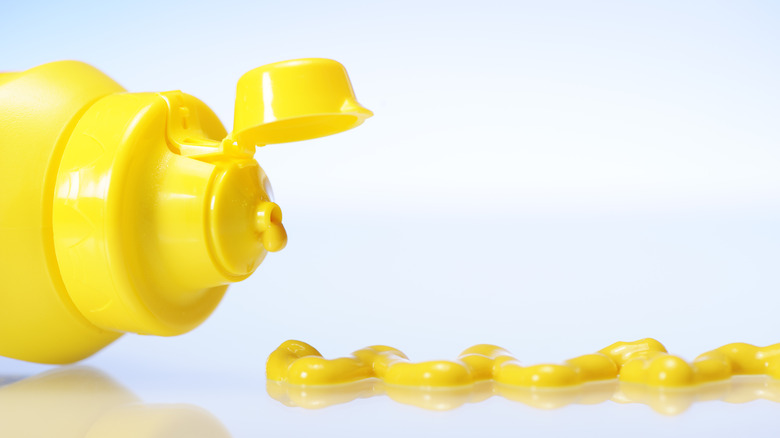 Yellow squirt bottle of mustard and mustard drips