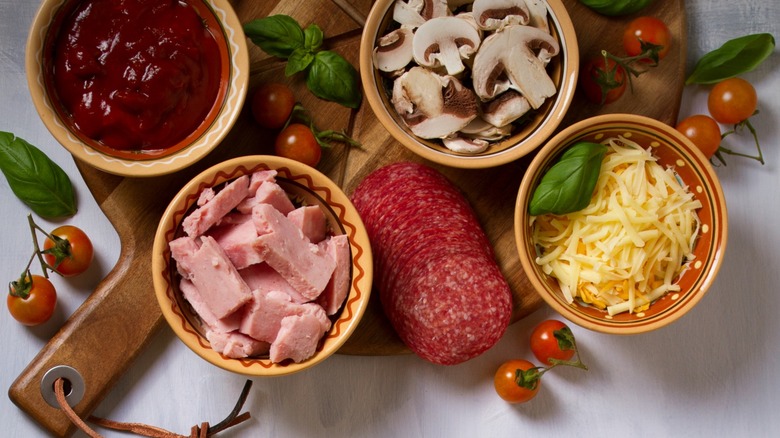 Pizza toppings including sauce, cheese, mushrooms, herbs, meat, tomatoes