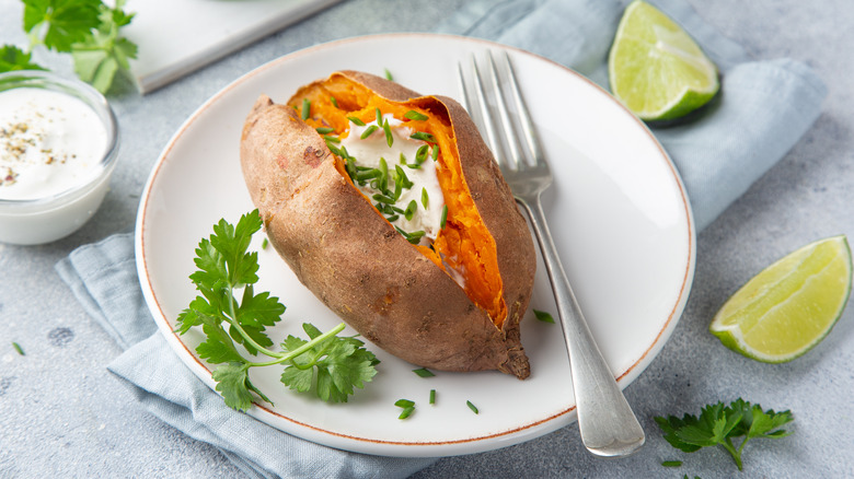 Baked sweet potato on white plate topped with sour cream and chives