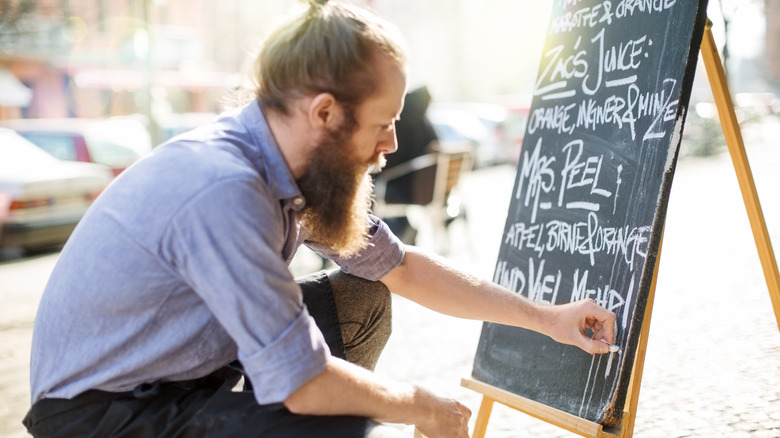 Person writing specials on menu chalkboard