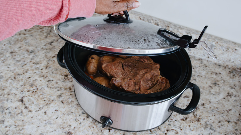 Hand lifting off a crock pot full of meat and veggies