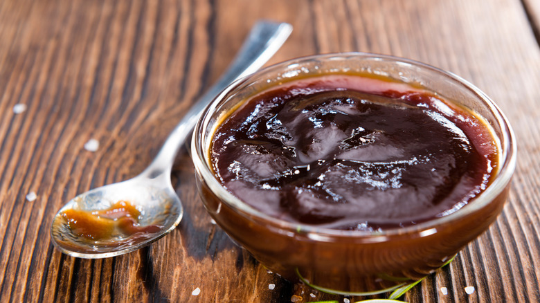 BBQ sauce in bowl with spoon on wooden table.