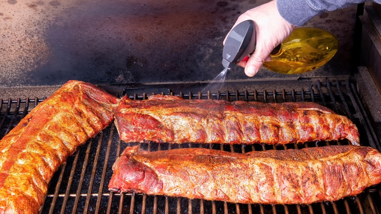 Spraying meat on barbecue with spray bottle