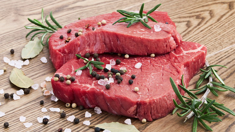 Raw steak with salt crystals, bay leaves, peppercorns, and sprigs of rosemary