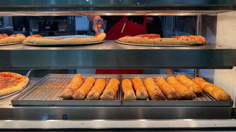 Costco food court pizzas and chicken bakes sit under heat lamps