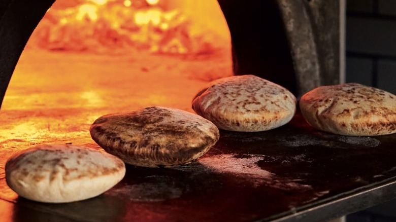 several homemade pita breads baking in an open wood fire oven