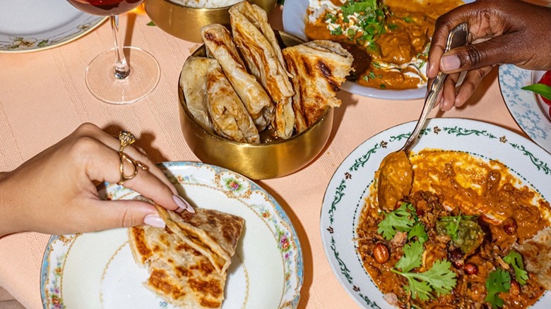 dinner table with hands dipping roti bread into plates of curry stew