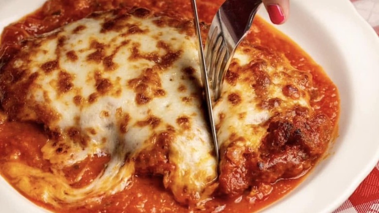 fork and knife cutting into a cheesy plate of chicken parmesan