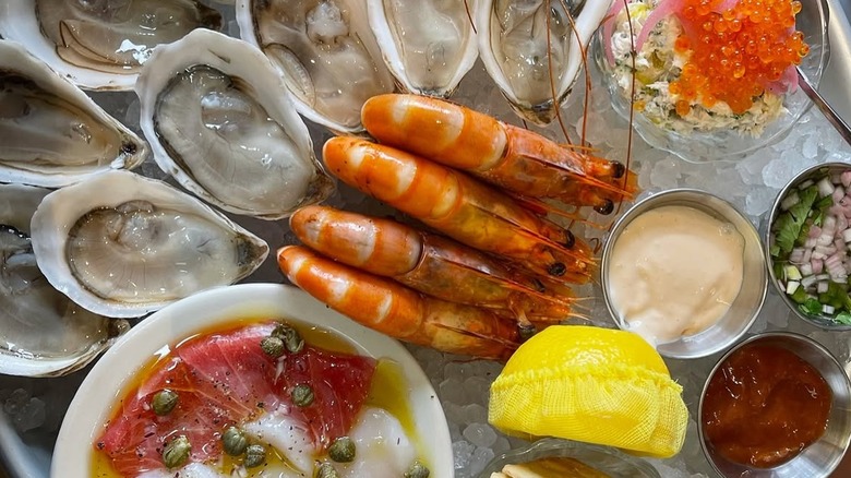 raw seafood platter on ice with shrimp, crudo, oysters, and various sauces