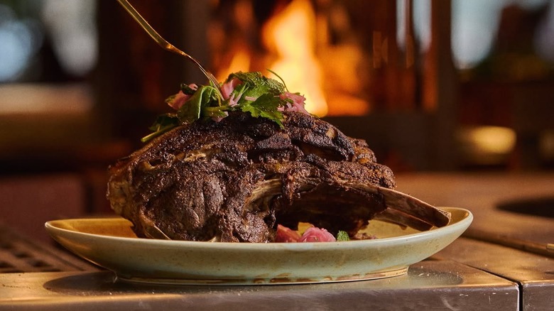 large plate of charred lamb shoulder sitting in front of an open wood fire