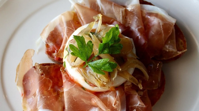 burrata on top of prosciutto and bread with caramelized onion and herbs on top