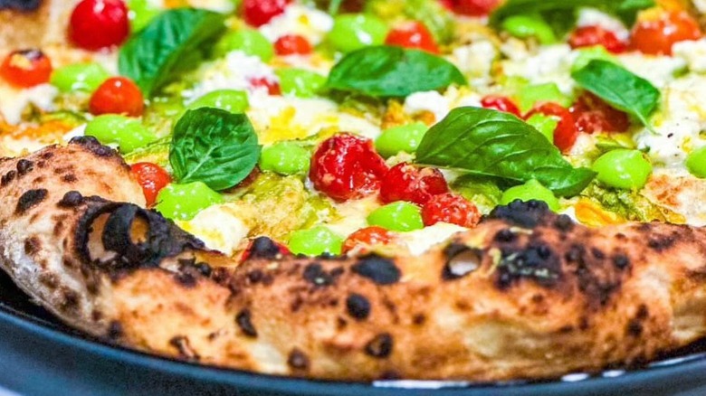 close up of pizza with charred crust, tomatoes, basil, cheese, and pesto