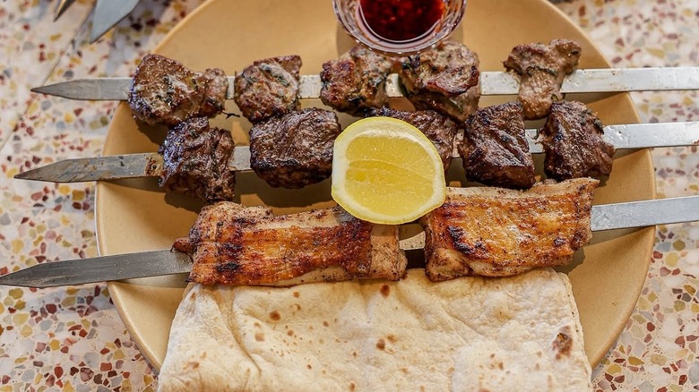 several pieces of meat on metal skewers with flat bread on top of a plate
