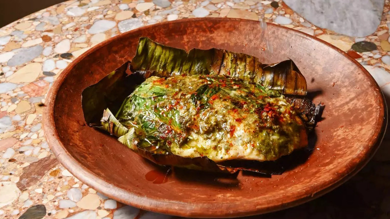 baked fish inside a banana leaf on a plate on top of a marble countertop