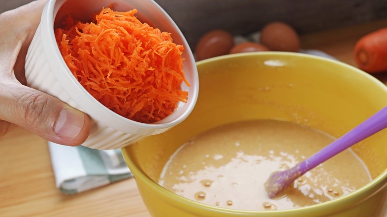 A person adding shredded carrots to cake batter