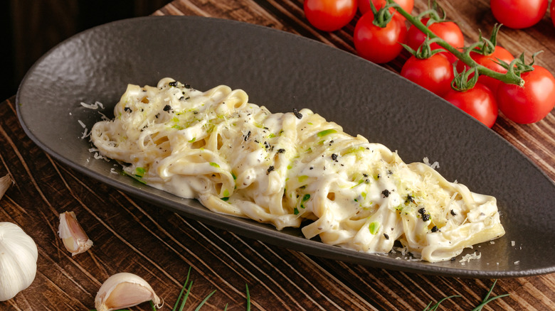 A black plate of pasta with a thick alfredo sauce.